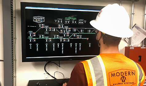 A worker sits at a control panel on a laptop.